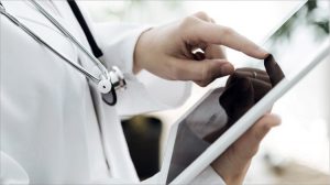Oberkörper in einem Arztkittel gekleidet und einem iPad in der Hand.