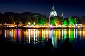 Blick auf das Rathaus von Hannover währen eines Festes am Abend mit bunten Lichtern die sich im Wasser spiegeln