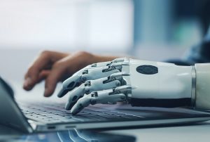 Schreiben am Laptop mit einer menschlichen Hand und einer Maschinen- bzw. Roboterhand